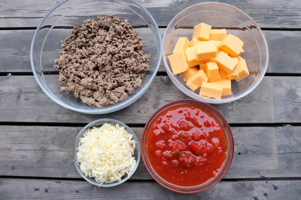 Rotel dip ingredients in clear bowls on a wooden table.