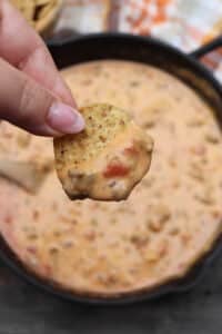 Chip with rotel dip being held over a skillet of cheesy rotel dip.