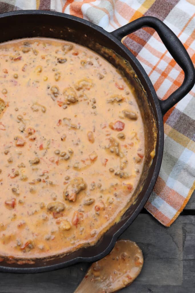 Cheese dip with ground beef, sausage and diced tomatoes in a skillet.
