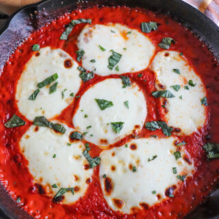 Mozzarella cheese slices on a bed of tomato sauce and chicken in a cast iron skillet.