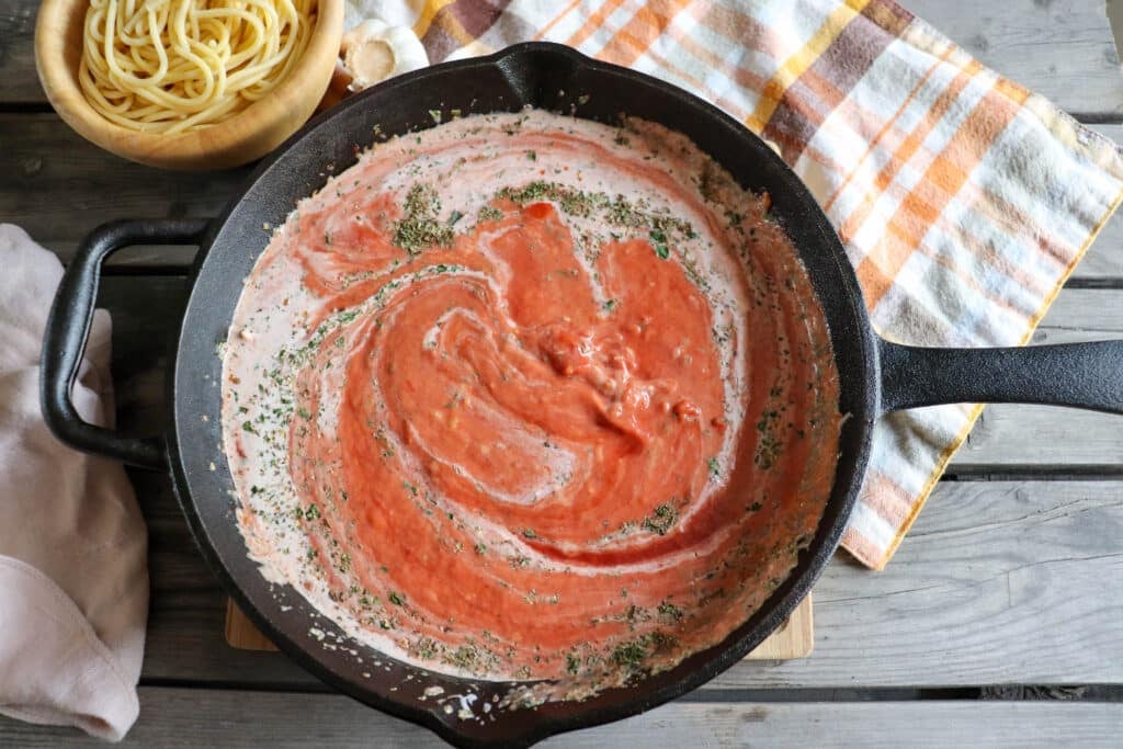 Crushed tomatoes swirled with cream and Italian seasoning in a cast iron pan.