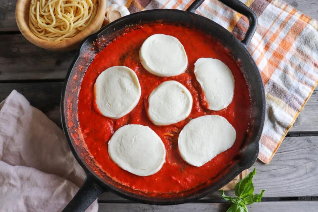 Tomato sauce topped with mozzarella slices in a cast iron skillet.