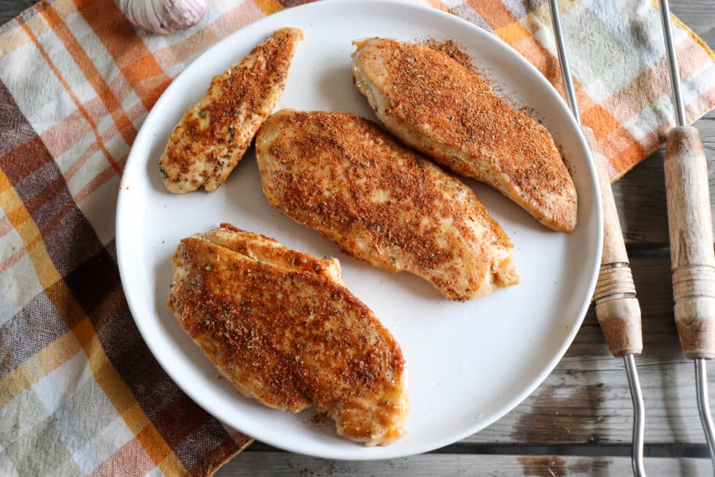 Chicken breasts coated in spices on a white speckled plate.