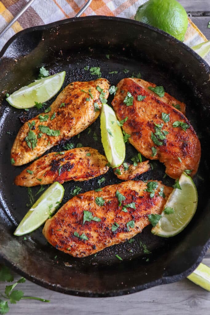 Blackened chicken breasts with lime wedges in a cast iron skillet with cilantro garnish.