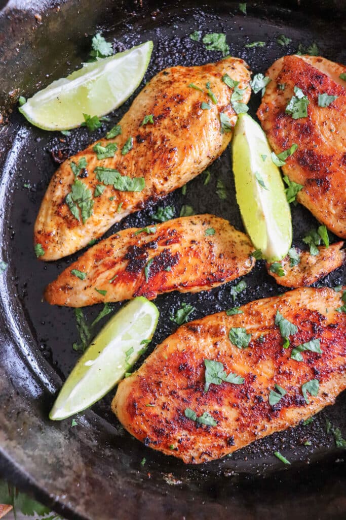 Blackened chicken breasts with lime wedges in a cast iron skillet with cilantro garnish.
