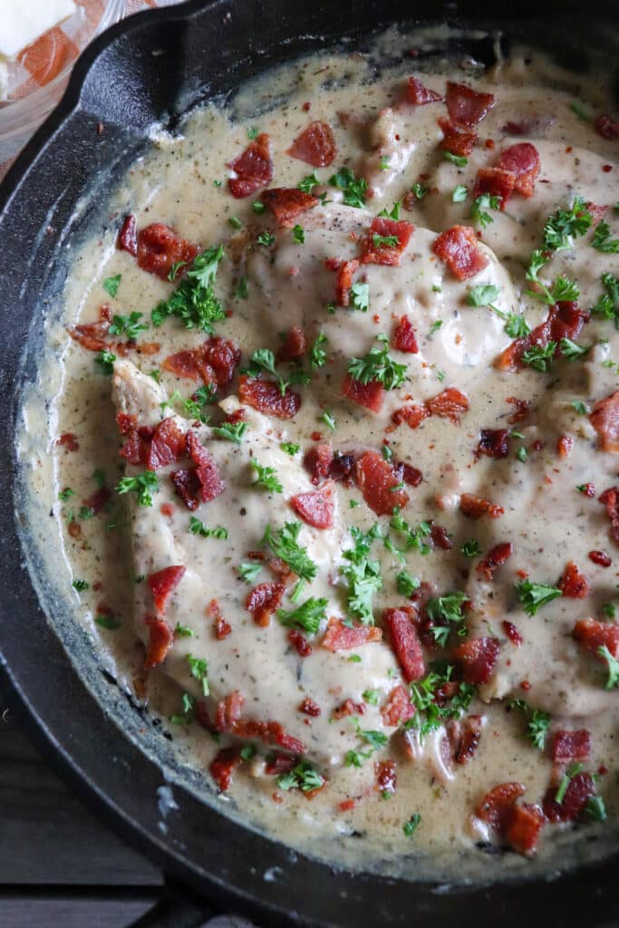 Chicken in a cream sauce with bacon and parsley garnish in a cast iron skillet.