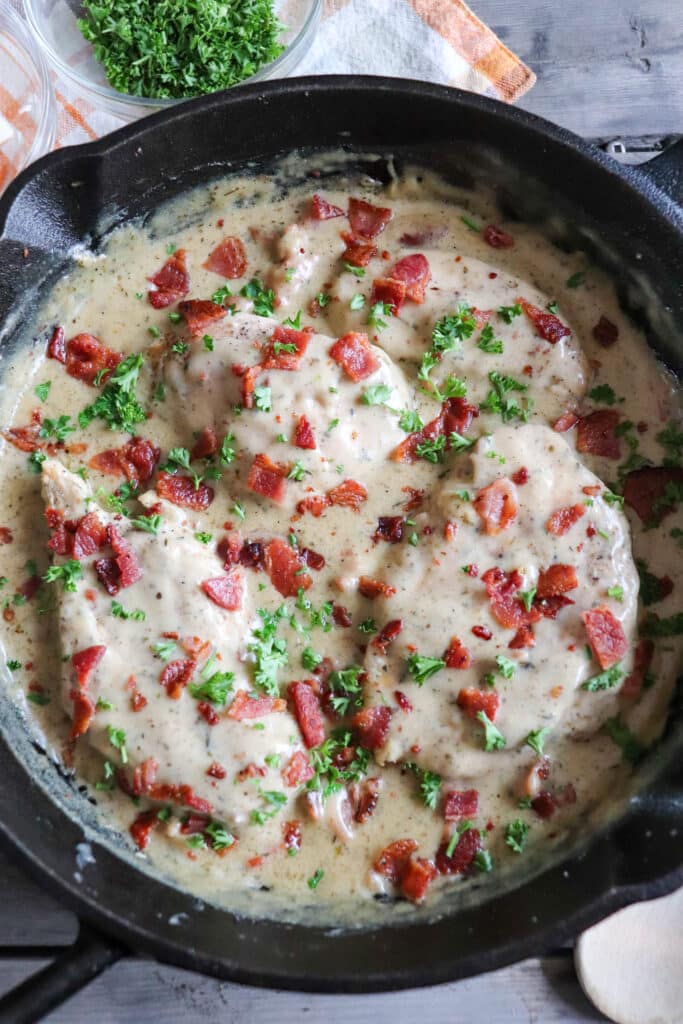 Chicken in a cream sauce with bacon and parsley garnish in a cast iron skillet.