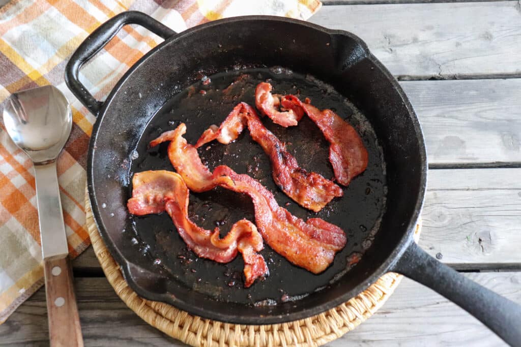 Four pieces of cooked bacon in a cast iron skillet.