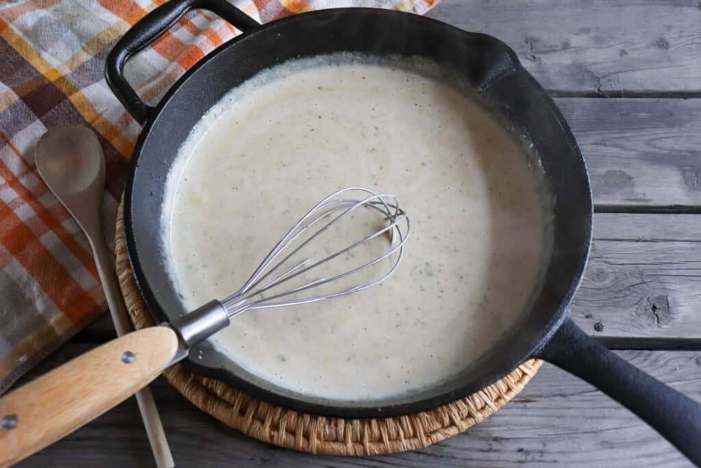 Creamy ranch sauce in a cast iron skillet with a whisk.
