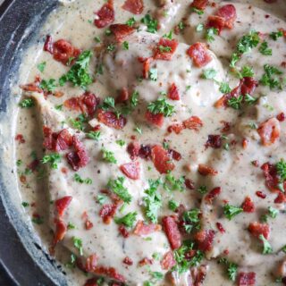 Chicken in a cream sauce with bacon and parsley garnish in a cast iron skillet.