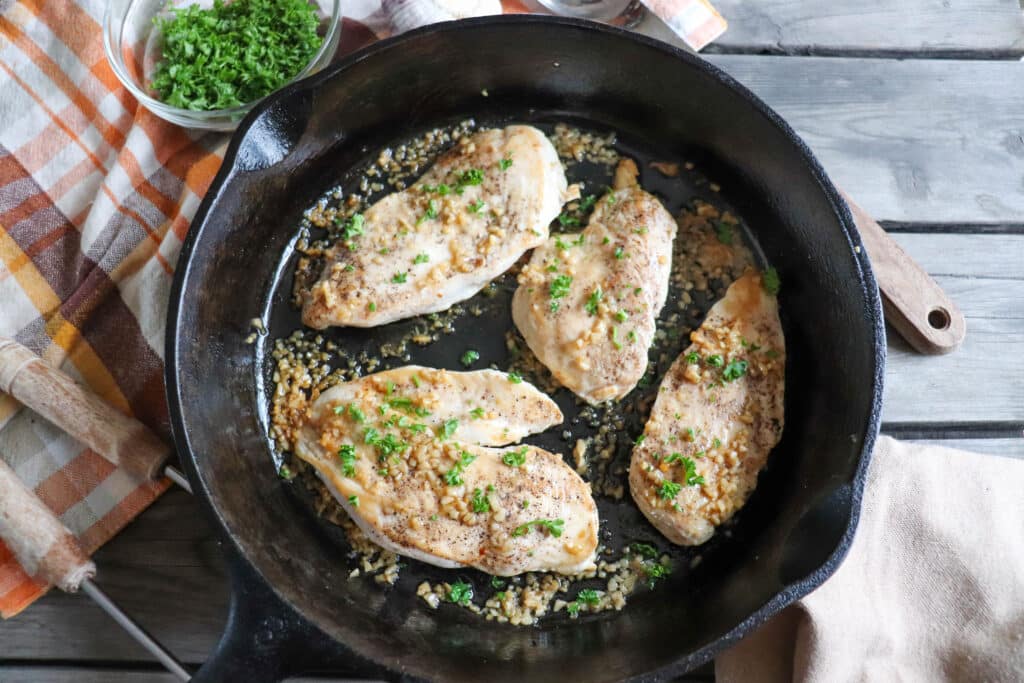 Cooked chicken breast garnished with minced garlic and parsley in a cast iron skillet.