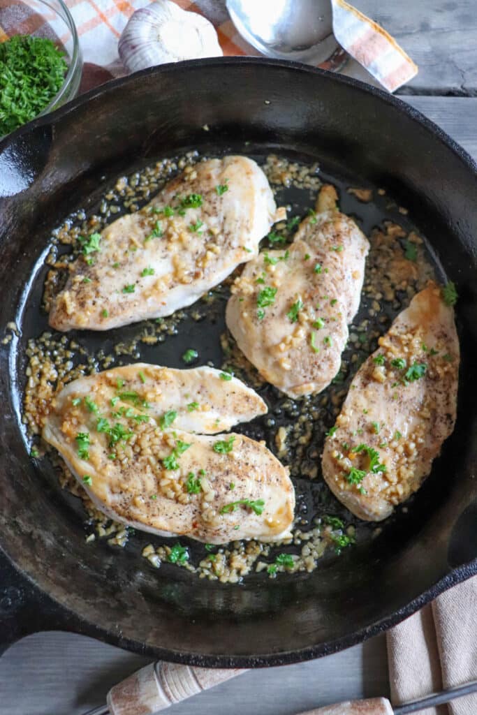 Cooked chicken breast garnished with minced garlic and parsley in a cast iron skillet.