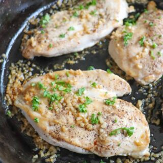 Cooked chicken breast garnished with minced garlic and parsley in a cast iron skillet.