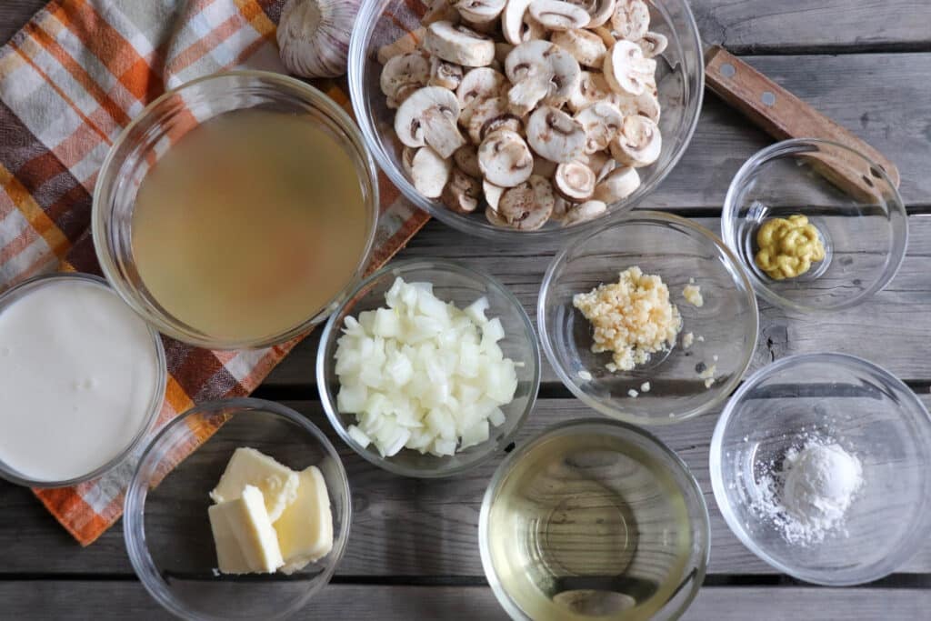 Ingredients for creamy mushroom chicken skillet in clear glass bowls on a wooden table.