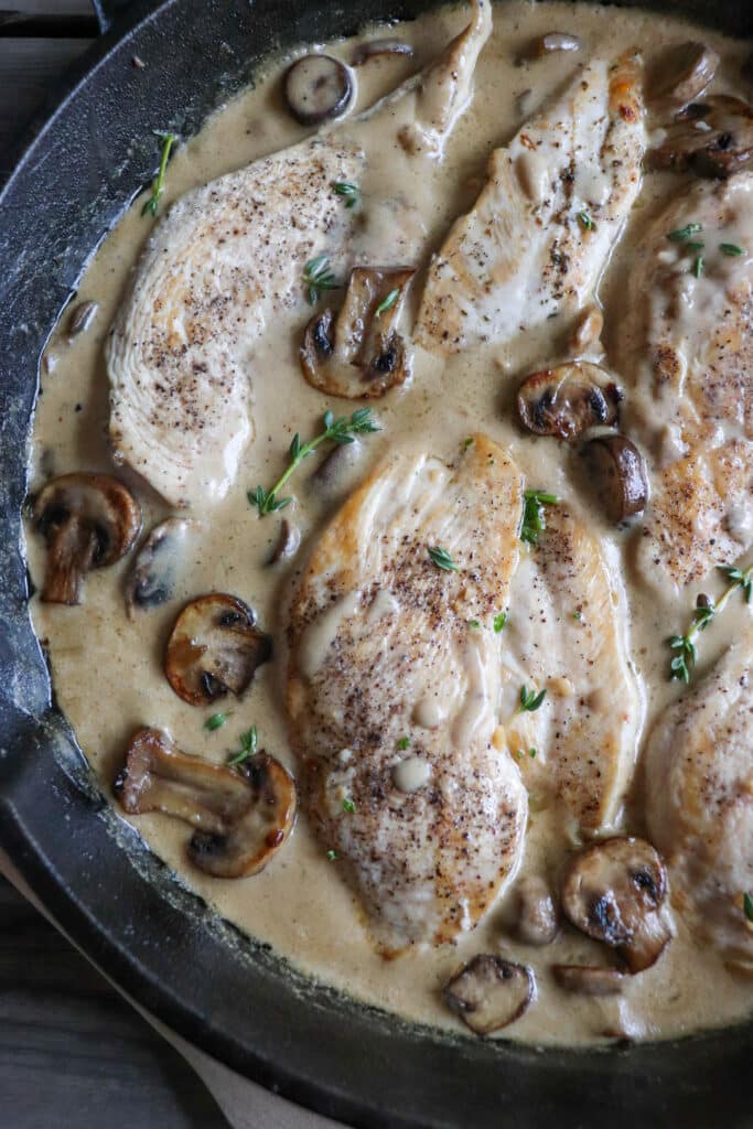 Cooked chicken breasts covered in a cream sauce with mushrooms in a cast iron skillet.
