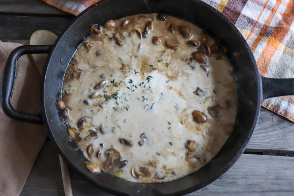 Cream and mushrooms with spices simmering in a cast iron skillet.