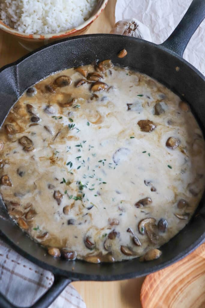 Cream and mushrooms with spices simmering in a cast iron skillet.