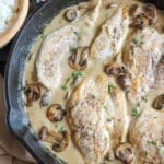 Cooked chicken breasts covered in a cream sauce with mushrooms in a cast iron skillet.
