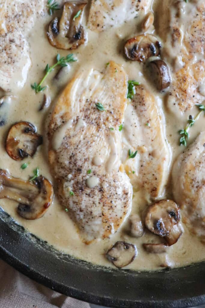 Close up of cooked chicken breast covered in a cream sauce with mushrooms in a cast iron skillet.