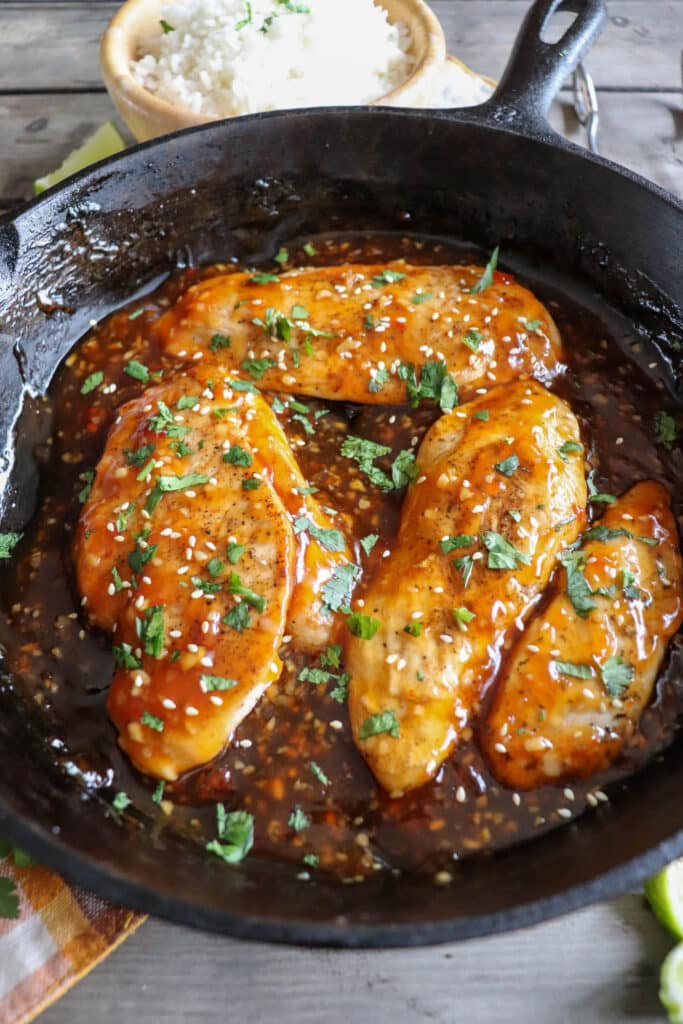 cooked chicken breast covered in sweet chili sauce, garnished with cilantro and sesame seeds in a cast iron skillet.
