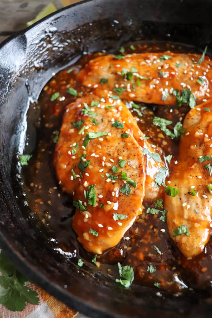 Cooked chicken breast covered in sweet chili sauce, garnished with cilantro and sesame seeds in a cast iron skillet.