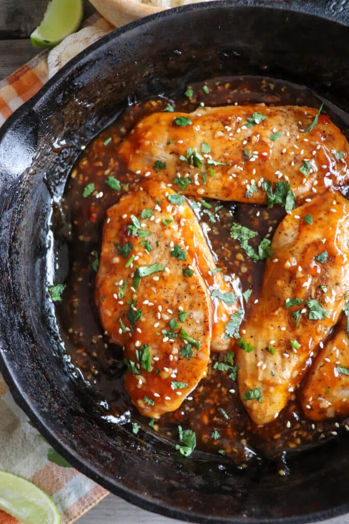 Cooked chicken breast covered in sweet chili sauce, garnished with cilantro and sesame seeds in a cast iron skillet.
