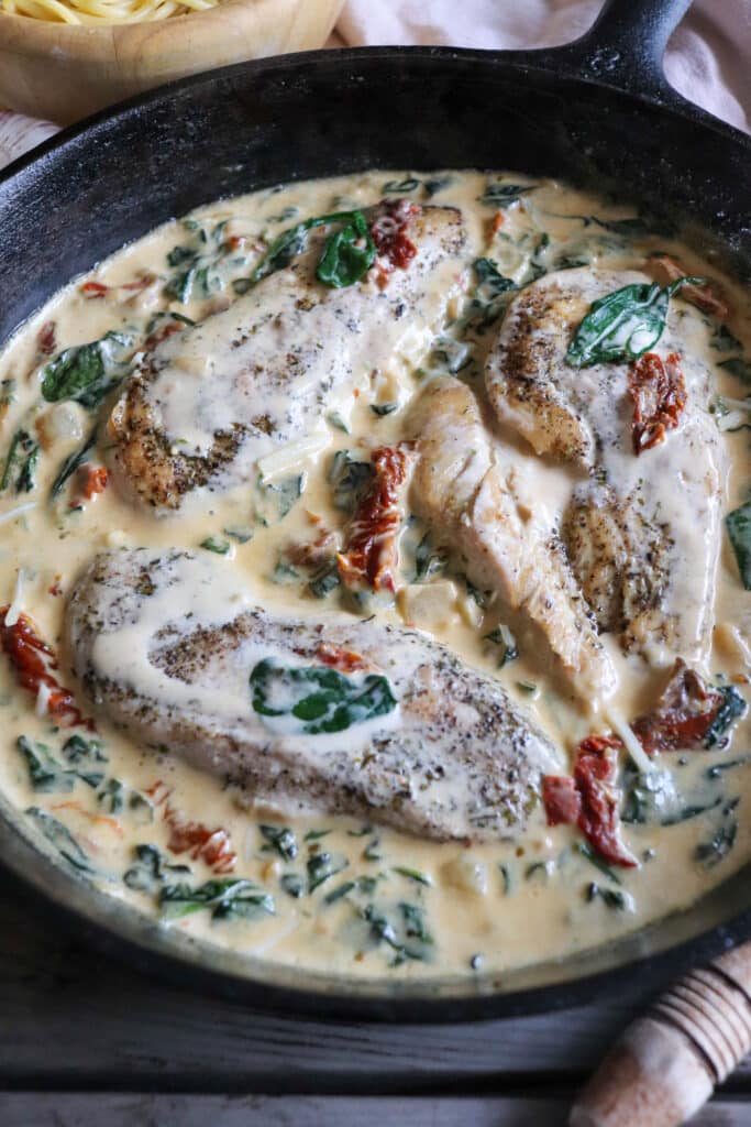 Cast iron skillet with chicken breast in a cream sauce with spinach and sun dried tomatoes.