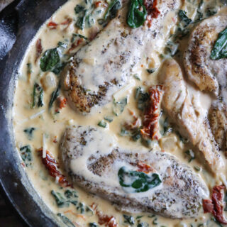 Cast iron skillet with chicken breast in a cream sauce with spinach and sun dried tomatoes.