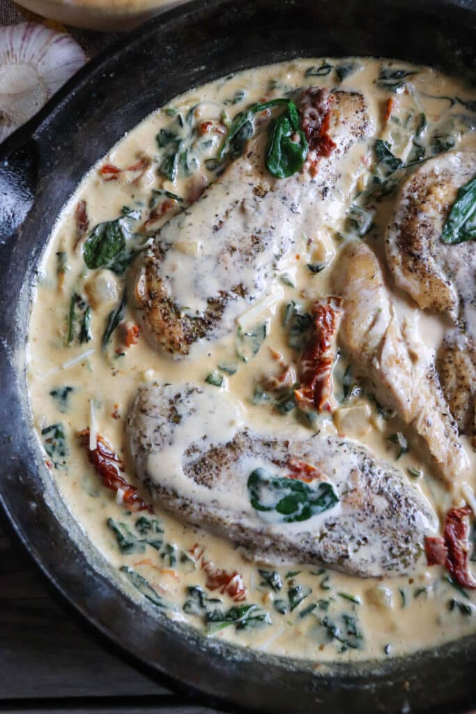 Cast iron skillet with chicken breast in a cream sauce with spinach and sun dried tomatoes.