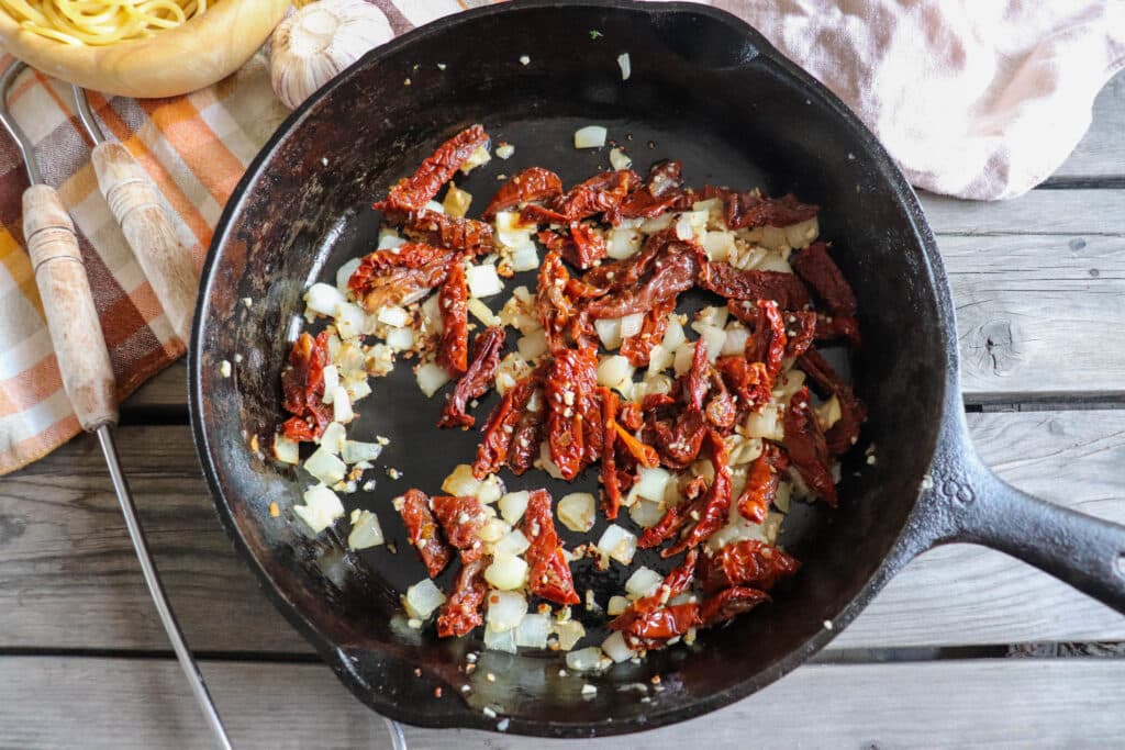 Onion, garlic and sun dried tomatoes in a cast iron skillet.
