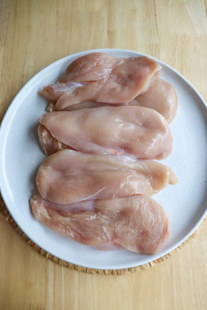 Raw chicken breasts on a speckled white plate.