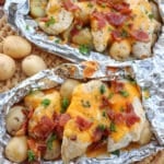 Chicken on small potatoes covered in bacon and melted cheese in foil packets.