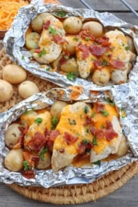 Chicken on small potatoes covered in bacon and melted cheese in foil packets.