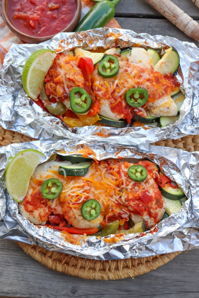 Salsa chicken in foil packets on a wooden picnic table.