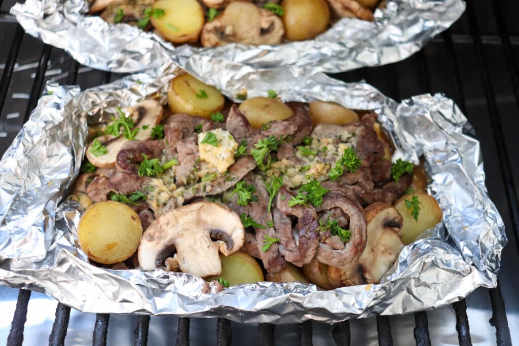 Steak, mushrooms and potatoes in a foil packet on the grill.