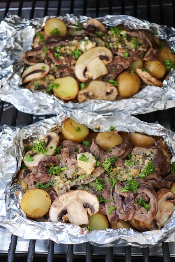 Steak, mushroom and potatoes in foil packets on the grill.