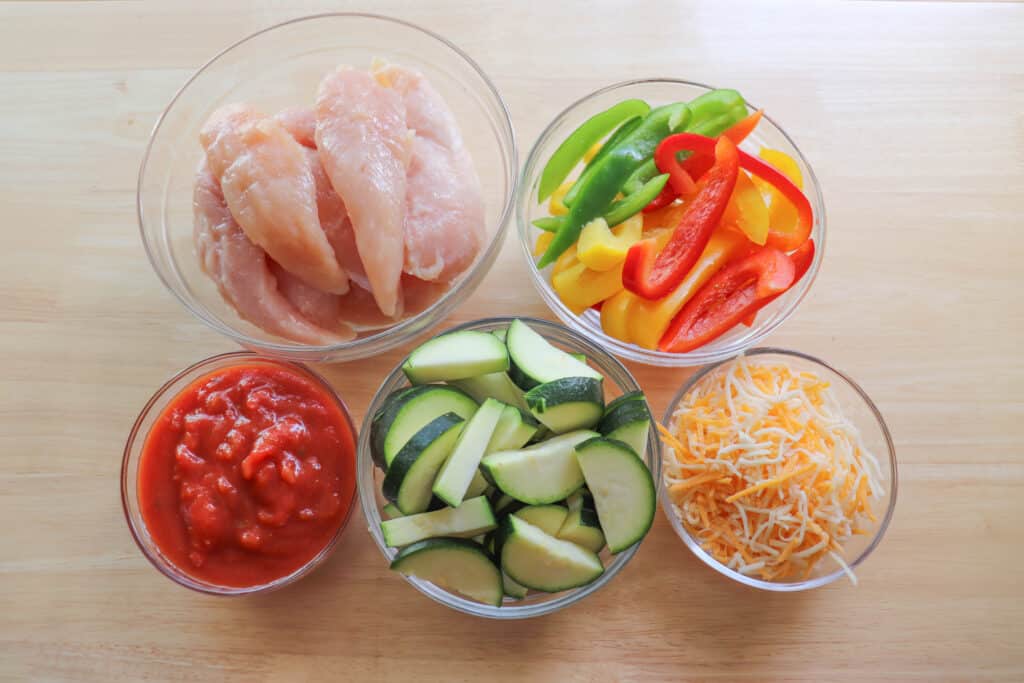 Salsa chicken ingredients in clear glass bowls on a wooden table.