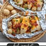 Two foil packets filled with ranch-seasoned chicken breasts topped with melted cheese, bacon bits, and small potatoes, garnished with parsley, placed on a woven mat. The text reads foil packet RANCH CHICKEN and CAMPFIREDOODIE.COM.