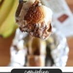 A spoonful of a banana boat dessert featuring toasted marshmallow and chocolate, with bananas and a blurry background. Text overlay reads Campfire Banana Boats with a website URL campfirefoodie.com.