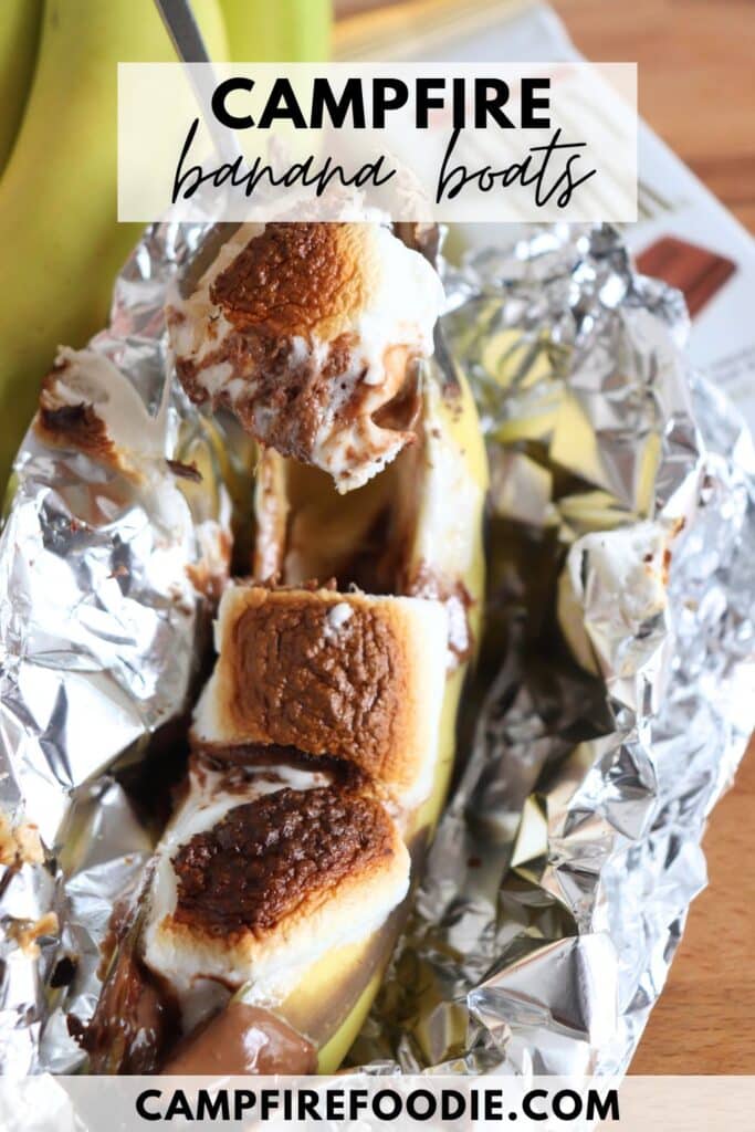 A banana boat dessert with toasted marshmallows and chocolate, wrapped in foil. A spoon is lifting a portion. The text CAMPFIRE banana boats and the website campfirefoodie.com are visible.