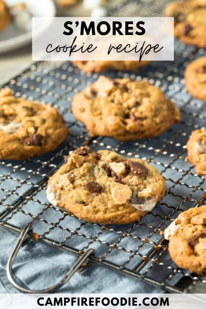 Freshly baked smores cookies with melted chocolate and marshmallows on a cooling rack. Text reads SMORES cookie recipe at the top and CAMPFIREEFOODIE.COM at the bottom.