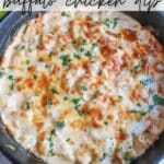 A skillet filled with creamy buffalo chicken dip topped with melted cheese and parsley. The dish has a golden, bubbly appearance. Text at the top reads Camping Skillet Buffalo Chicken Dip and at the bottom campfirefoodie.com.