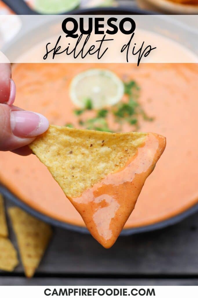 A close-up of a hand holding a triangular tortilla chip dipped in creamy queso skillet dip. The dip is smooth and orange with a garnish in the background. Text at the top reads QUESO skillet dip, and the bottom text says CAMPFIREDOODIE.COM.