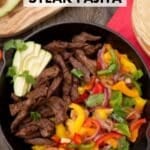 A skillet filled with steak strips, colorful bell peppers, onions, and garnished with cilantro. Slices of avocado are placed on top. A wooden board with avocado slices and other toppings is in the background. Text reads Skillet Steak Fajita.