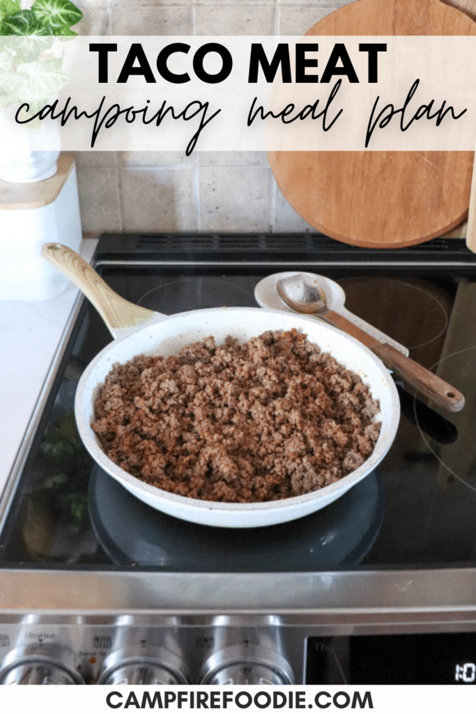 A frying pan on a stove contains cooked ground taco meat. A wooden spoon rests on the pans handle. The background shows a portion of a kitchen counter with a cutting board. Text at the top reads Taco Meat Camping Meal Plan.