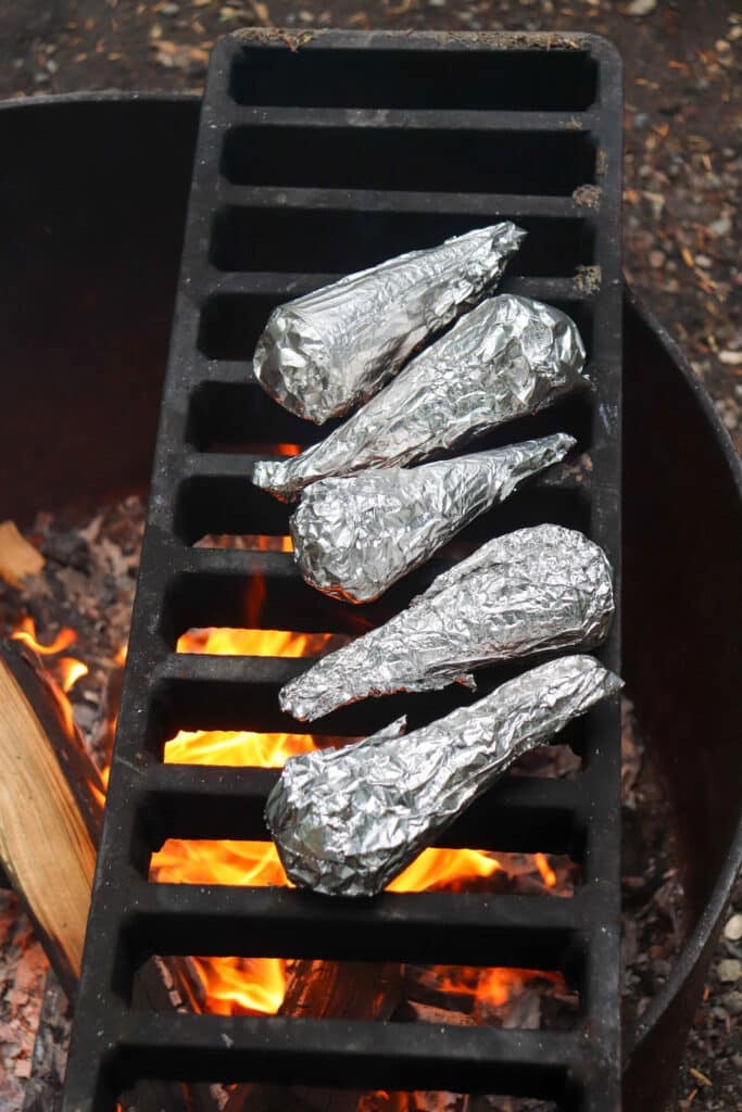 Cones wrapped in foil on the grate of an open fire.