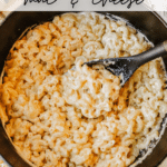 A black pot filled with creamy macaroni and cheese, being stirred with a black spoon. The top is golden and slightly browned. The text Dutch Oven Mac & Cheese and Campfire Foodie is overlaid.