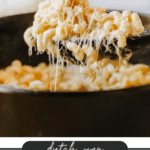 A spoonful of creamy, gooey macaroni and cheese is lifted from a Dutch oven, showcasing the stretchy melted cheese. Text on the image reads: Dutch Oven Macaroni & Cheese, campfirefoodie.com.