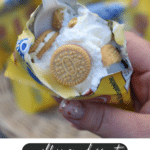 A hand holding an opened mini lemon Oreo cookie packet filled with whipped cream, two mini lemon Oreos, and a plastic spoon. Text at the bottom reads: walking dessert Lemon Meringue Pie campfirefoodie.com.
