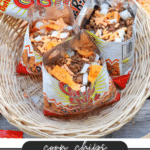 Three open bags of corn chips filled with seasoned ground beef, shredded cheese, and chopped onions, arranged in a woven basket. Text overlay reads: “corn chips WALKING TACOS campfirefoodie.com.”.